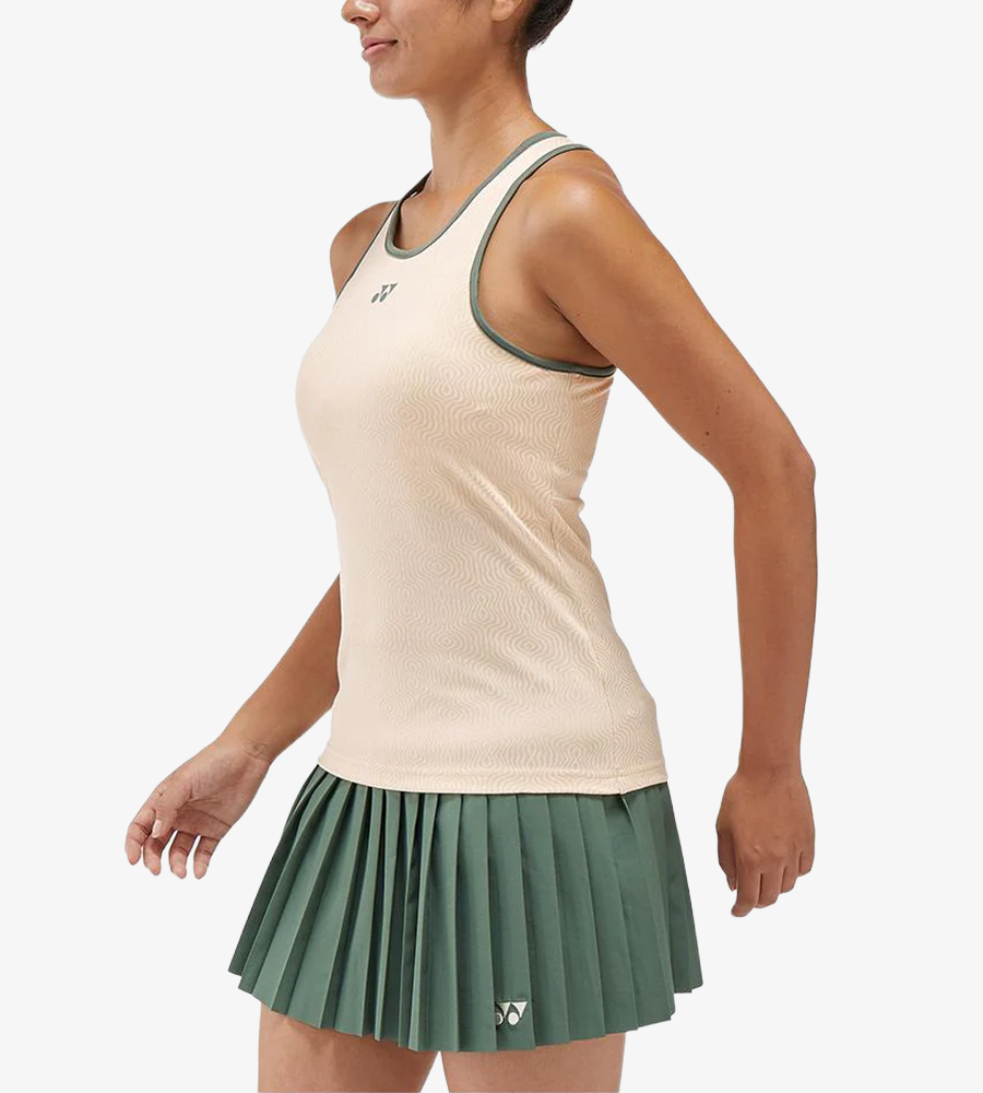 模特兒穿著 Yonex 20757 杏色女裝運動背心配襯綠色滾邊及百褶裙。 | Woman wearing a peach-colored Yonex 20757 Women's Tank Top with green trim and a matching pleated green skirt.